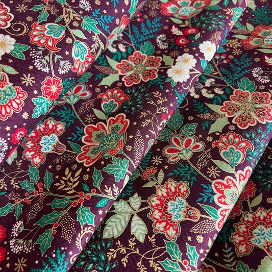A close-up of draped fabric with an intricate floral and botanical print on a dark burgundy background, featuring red, green, gold, teal, and cream motifs.