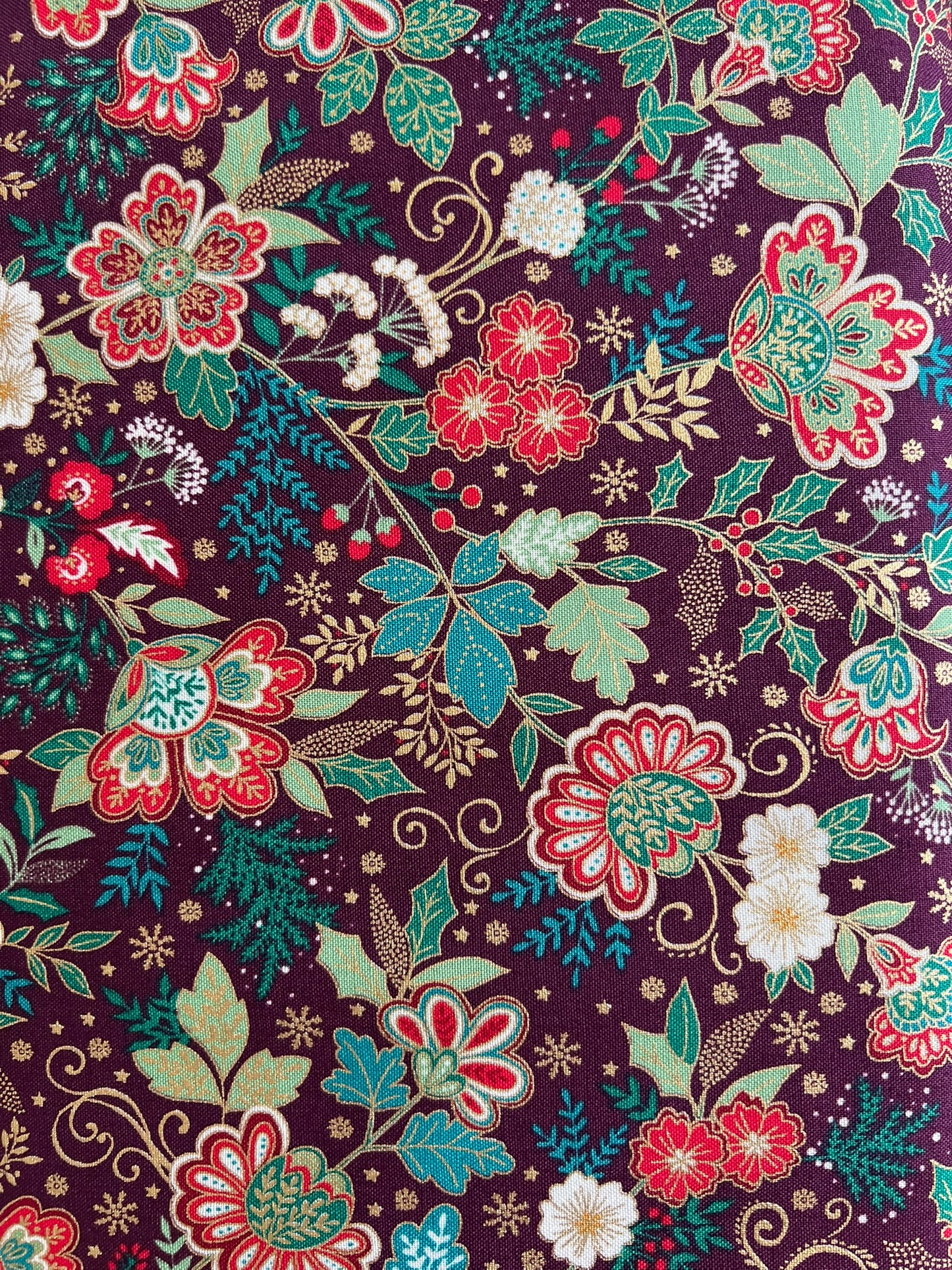 A close-up of a floral fabric pattern featuring red, teal, and white flowers with green leaves on a dark purple background.