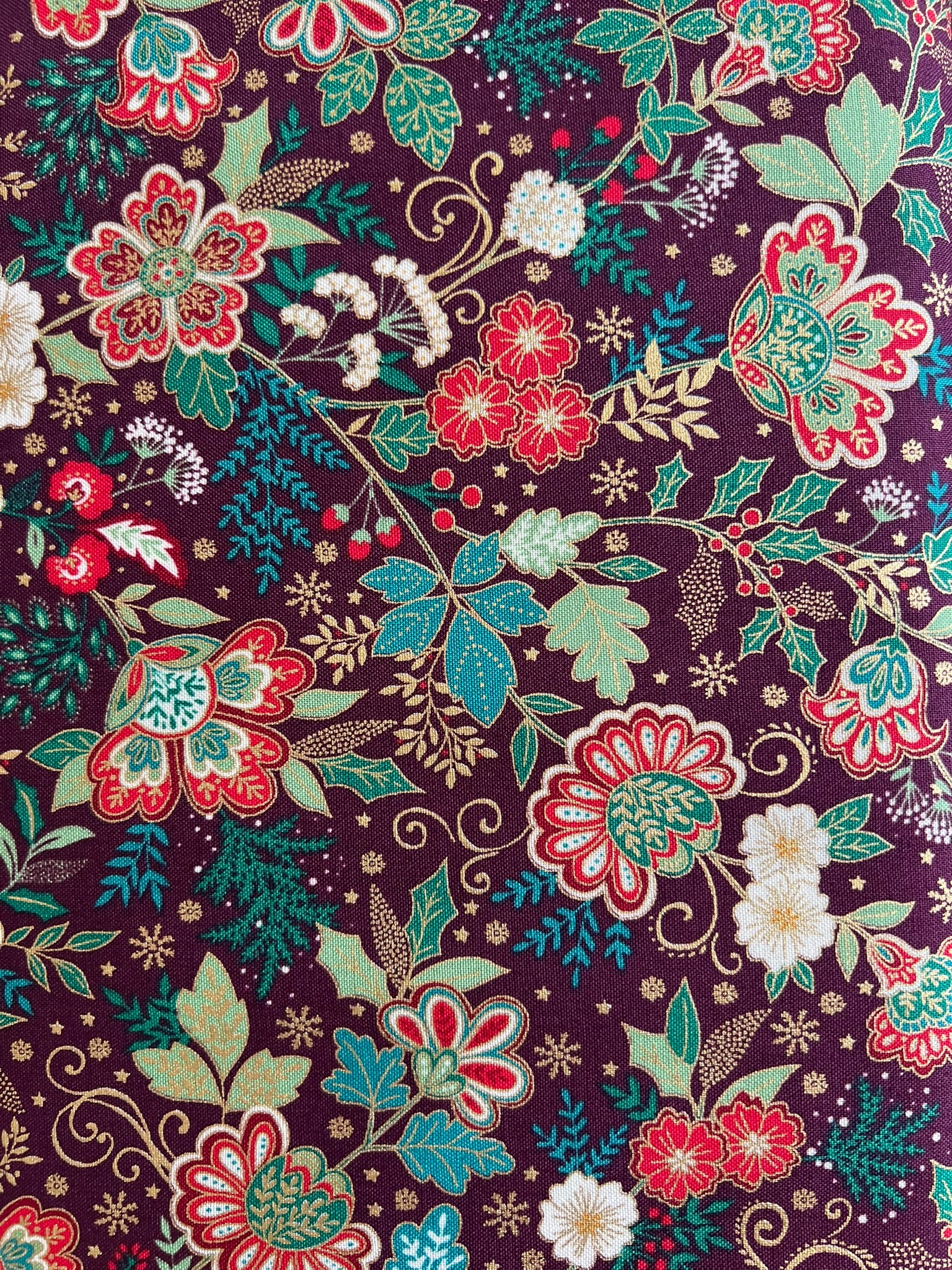 A close-up of a floral fabric pattern featuring red, teal, and white flowers with green leaves on a dark purple background.