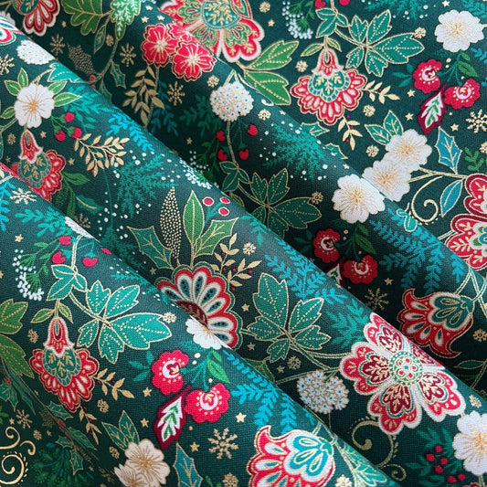A close-up of a folded fabric with a dense floral and botanical print on a dark teal-green background. The pattern features red, pink, and white flowers, light green leaves, and small gold star-like accents.