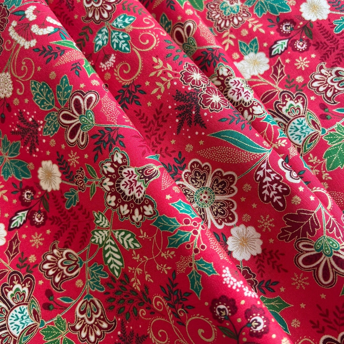 A close-up of a draped red fabric with an intricate floral and botanical print in green, white, brown, and gold.