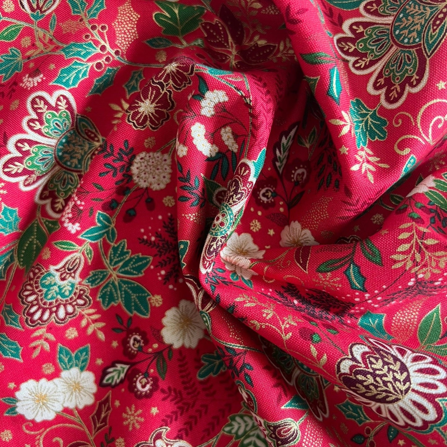 A close-up of draped red fabric with a detailed floral and botanical block print pattern in green, white, and gold.