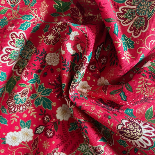 A close-up of draped red fabric with a detailed floral and botanical block print pattern in green, white, and gold.