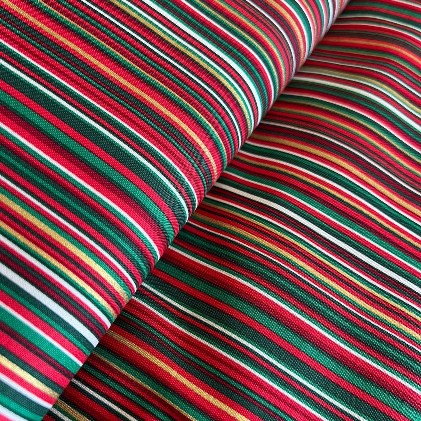 A close-up of striped fabric with alternating bands of red, green, black, white, and thin yellow lines, shown folded to display the pattern and texture.