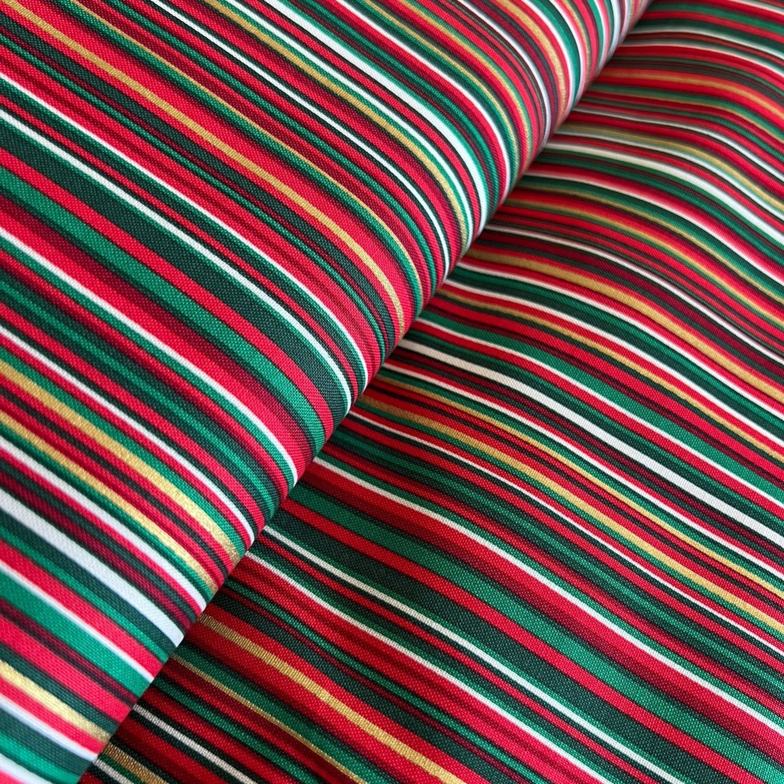 A close-up of striped fabric with alternating bands of red, green, black, white, and thin yellow lines, shown folded to display the pattern and texture.