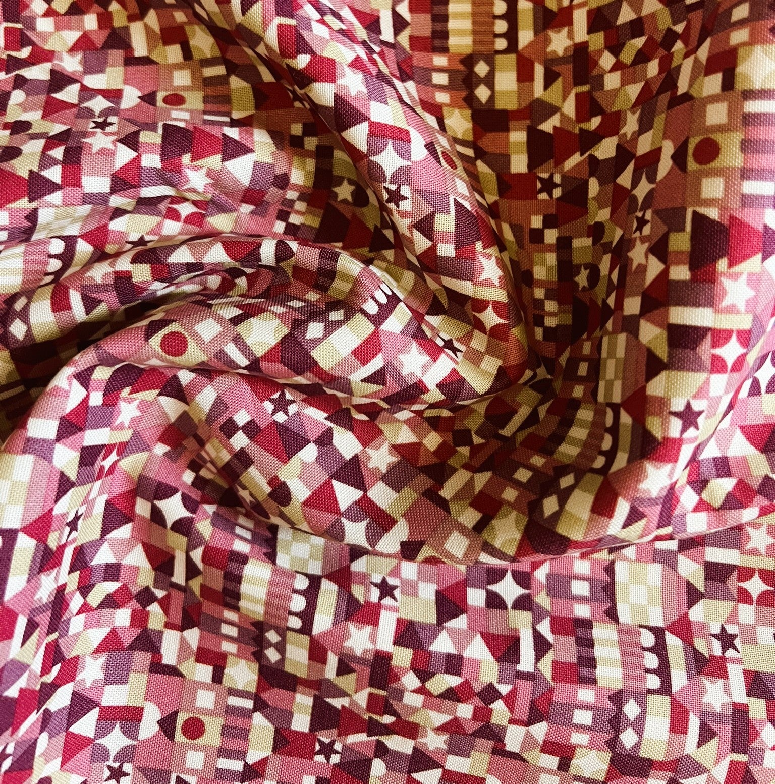 A close-up of draped fabric with an all-over geometric pattern in red, burgundy, cream, and brown.