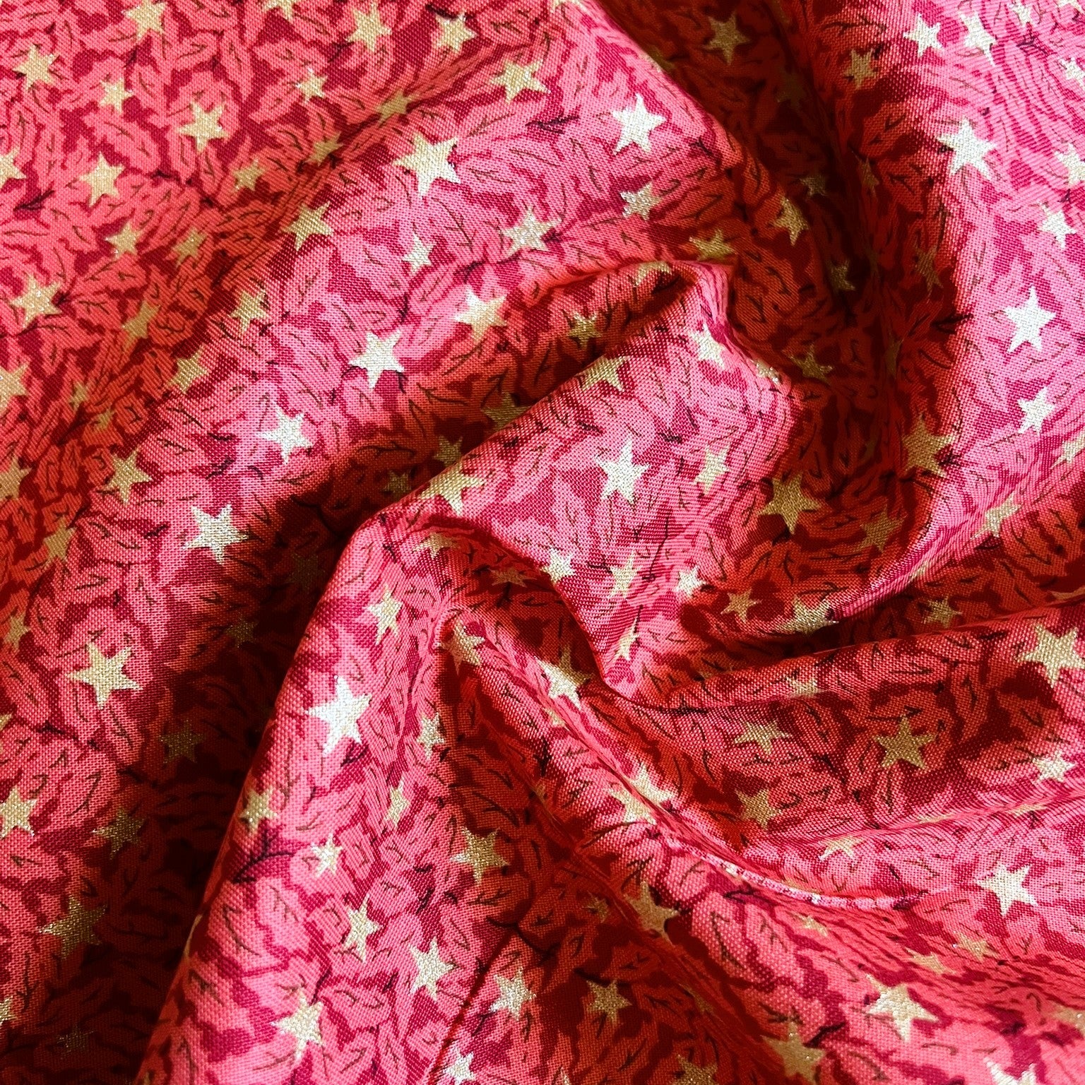 A close-up of draped pink fabric with an allover pattern of small white stars and darker red leaf-like motifs.
