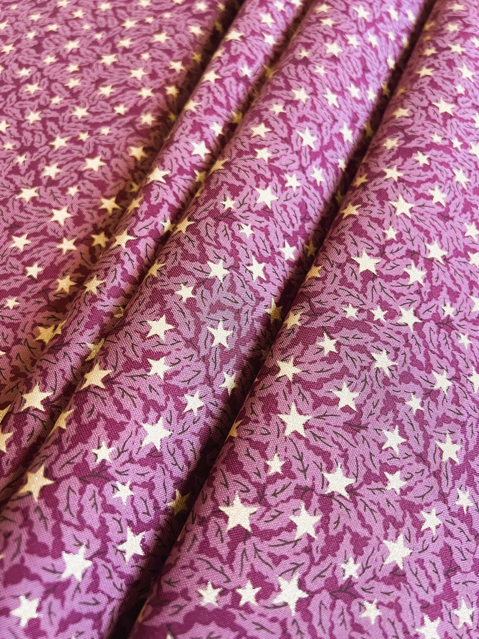 A close-up of a purple fabric with a repeating pattern of white stars and small gold accents, draped in soft folds.