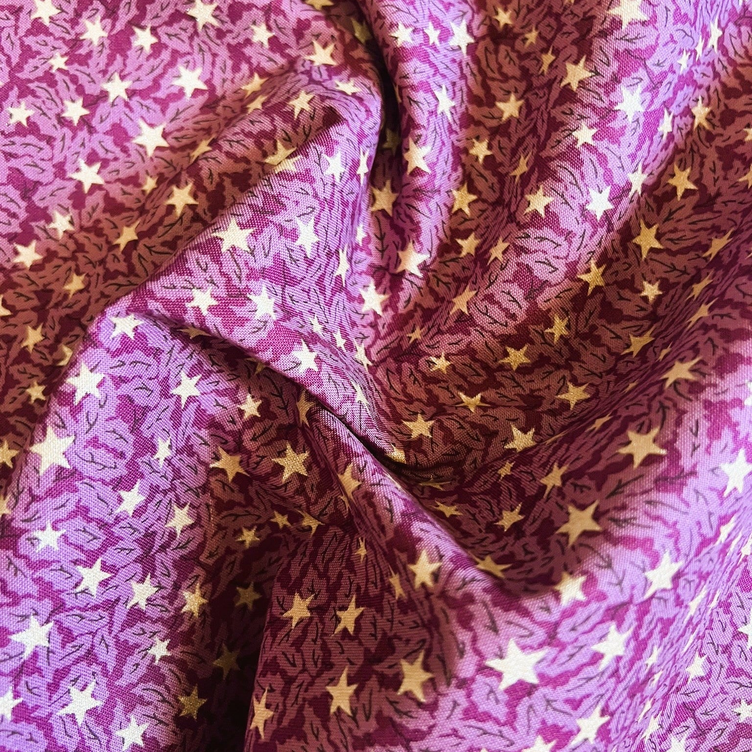 A close-up of draped fabric with a repeating pattern of small yellow stars over a magenta and purple background.