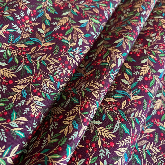 A close-up of draped fabric with an all-over botanical print featuring burgundy berries, green and metallic gold leaves, and tan foliage on a dark burgundy background.