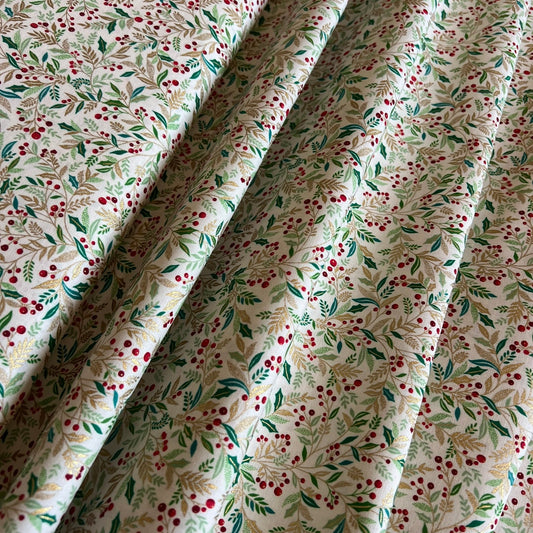 A close-up of draped fabric with a delicate botanical print featuring gold metallic and green leaves and small red berries on an off-white background.