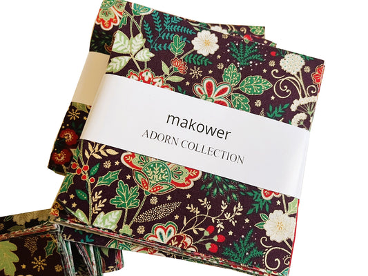 A stack of fabric swatches from the makower Adorn Collection, featuring a dark brown background with a detailed botanical pattern in green, red, and cream, wrapped with a white paper band.
