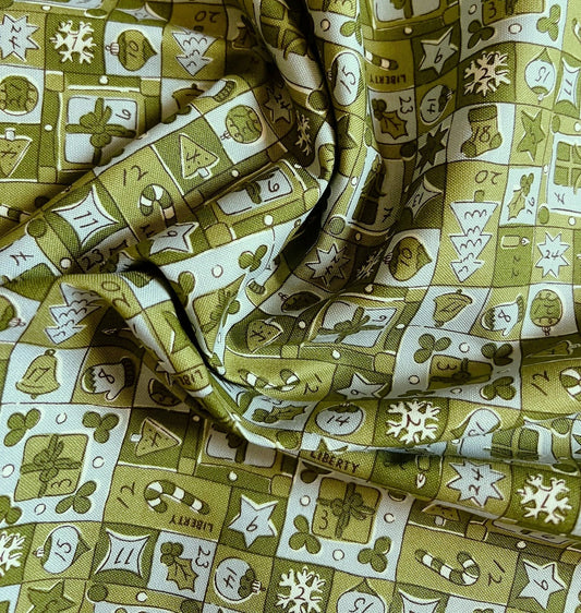A close-up of draped fabric with a repeating holiday-themed print in olive green, cream, and brown, featuring ornaments, candy canes, snowflakes, and the word Liberty.