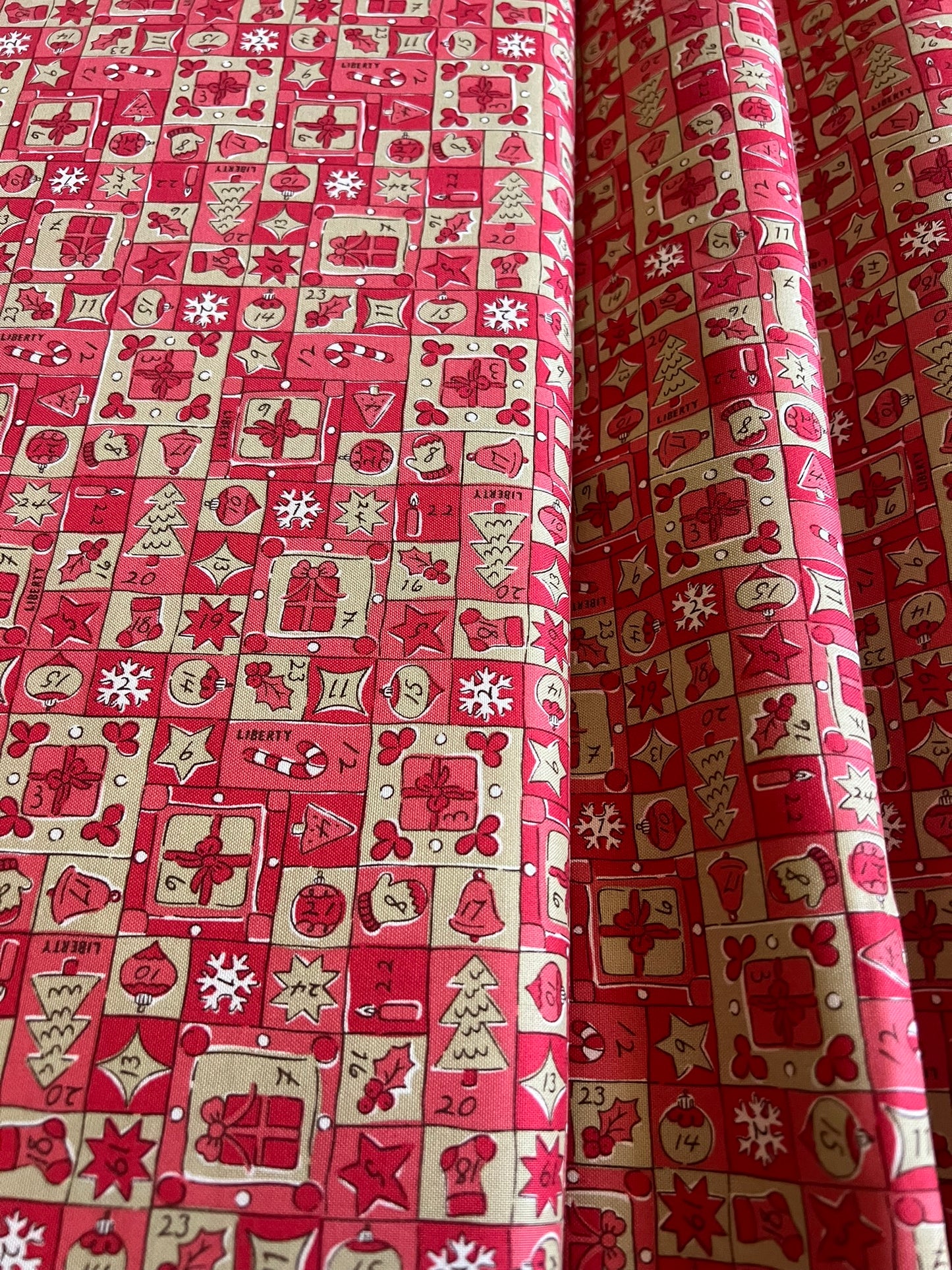 Red and cream Christmas-themed fabric with a repeating grid pattern of gift boxes, Santa Claus, snowflakes, candy canes, and holiday icons, shown folded to display its texture and pattern.