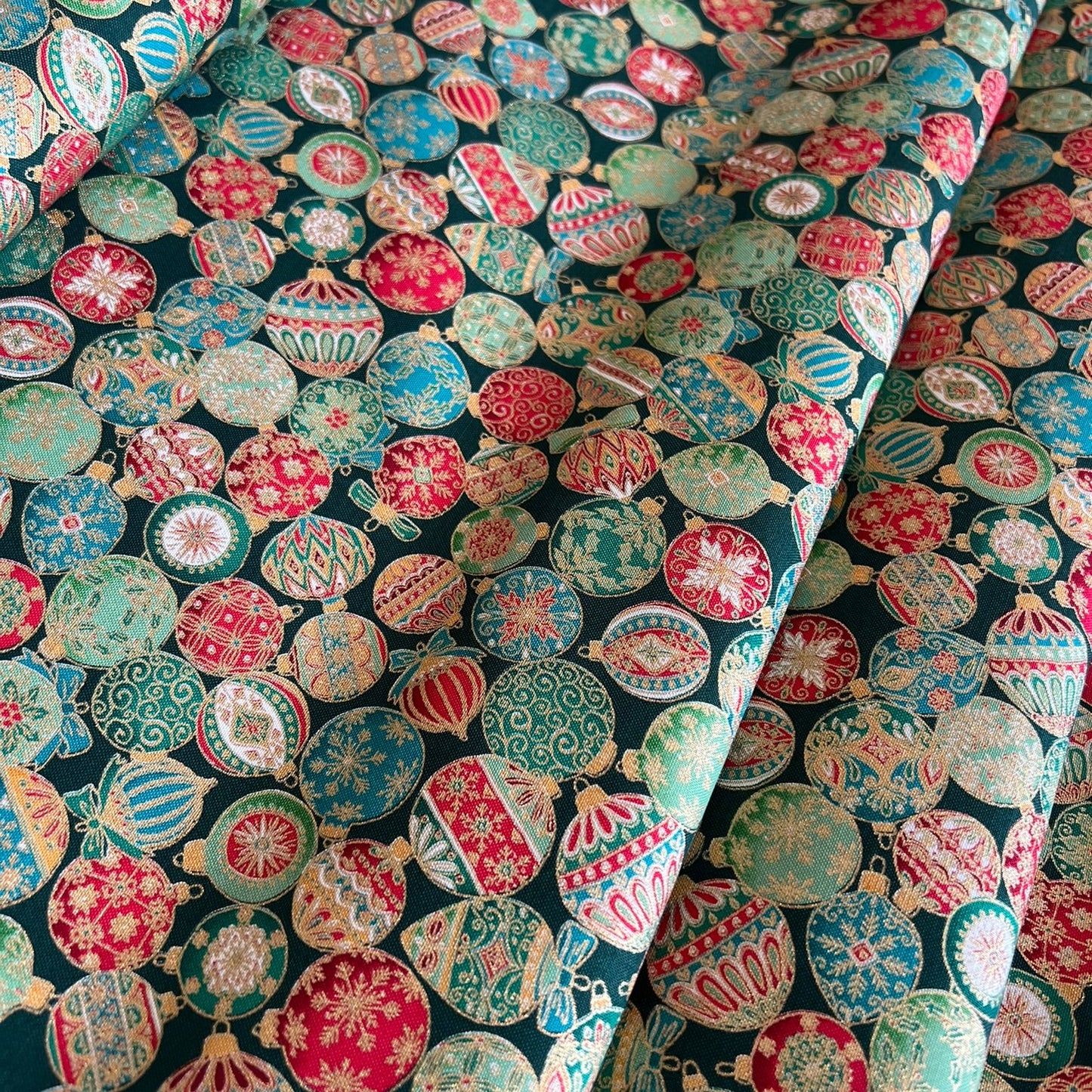 A close-up of patterned fabric with a dense arrangement of colorful Christmas ornaments in red, green, cream, and metallic gold on a dark background.