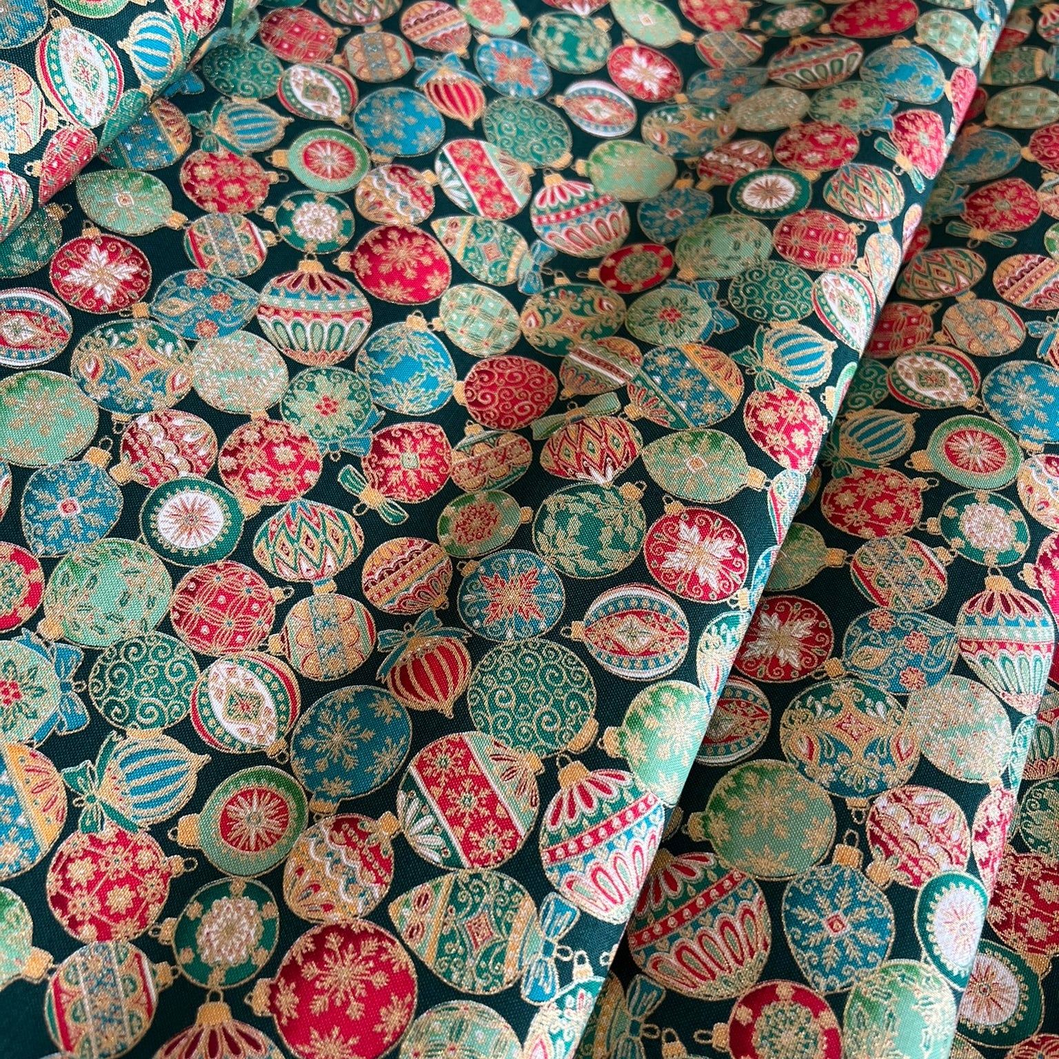 A close-up of patterned fabric with a dense arrangement of colorful Christmas ornaments in red, green, cream, and metallic gold on a dark background.