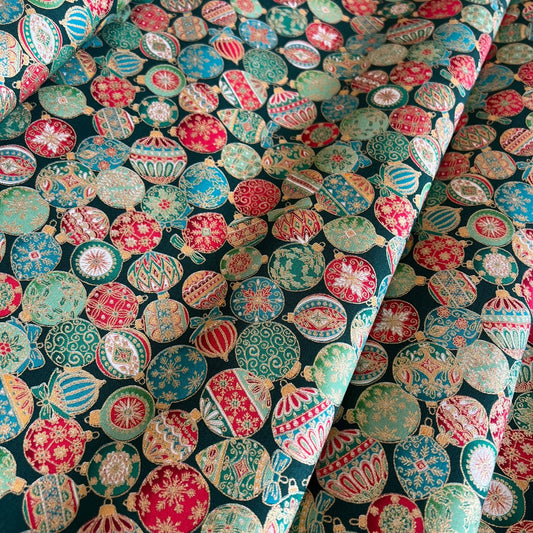 A close-up of patterned fabric with a dense arrangement of colorful Christmas ornaments in red, green, cream, and metallic gold on a dark background.