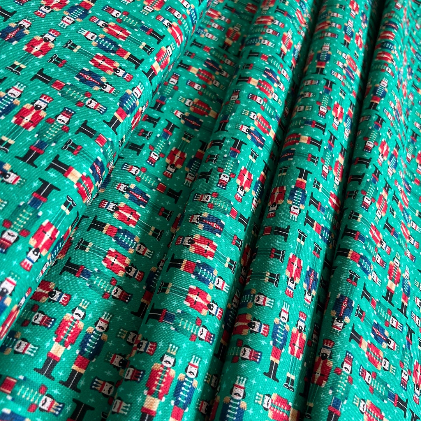 A close-up of a patterned fabric with a teal green background featuring a repeating print of red, white, and blue nutcracker soldiers.