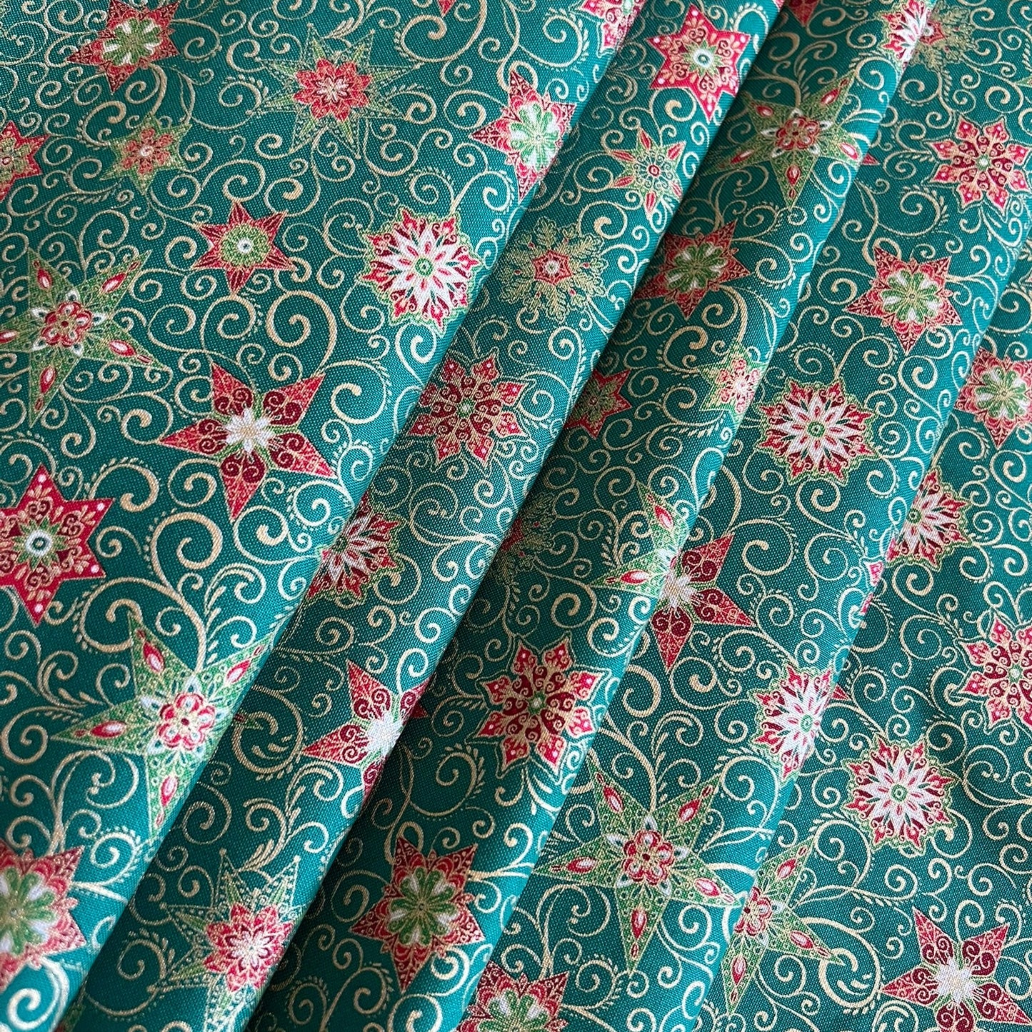 A close-up of draped green fabric with an all-over floral and scroll pattern in pink, white, and metallic gold.