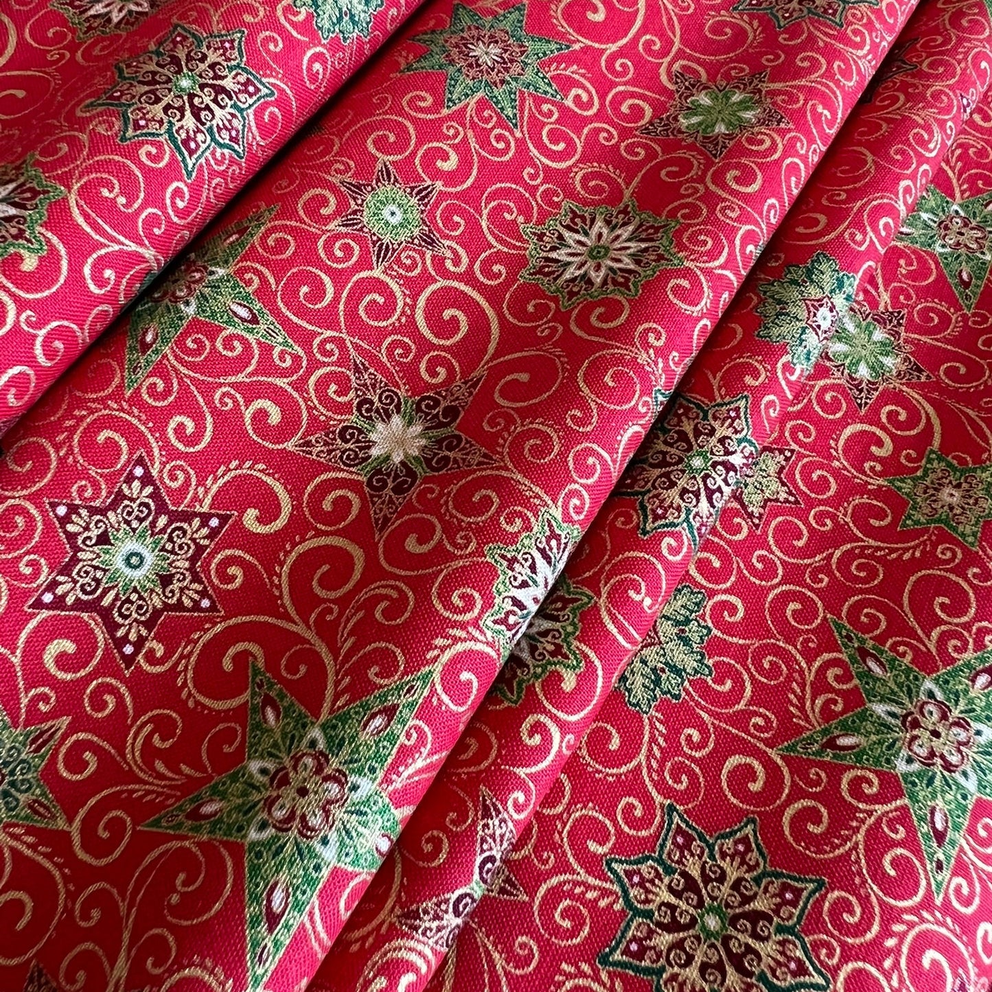 A close-up of folded red fabric with an allover printed pattern of cream swirls, green and metallic gold leaves, and multicolored floral medallions.
