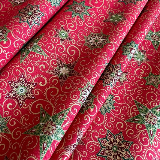 A close-up of folded red fabric with an allover printed pattern of cream swirls, green and metallic gold leaves, and multicolored floral medallions.