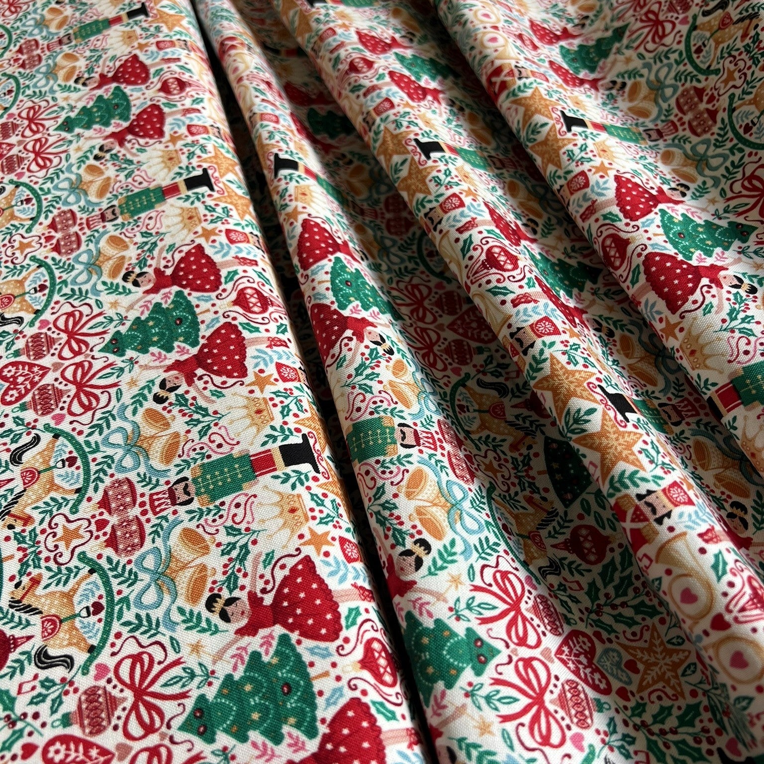 A close-up of draped fabric with a dense Christmas-themed print featuring red berries, green trees, ornaments, and floral motifs on a light cream background.