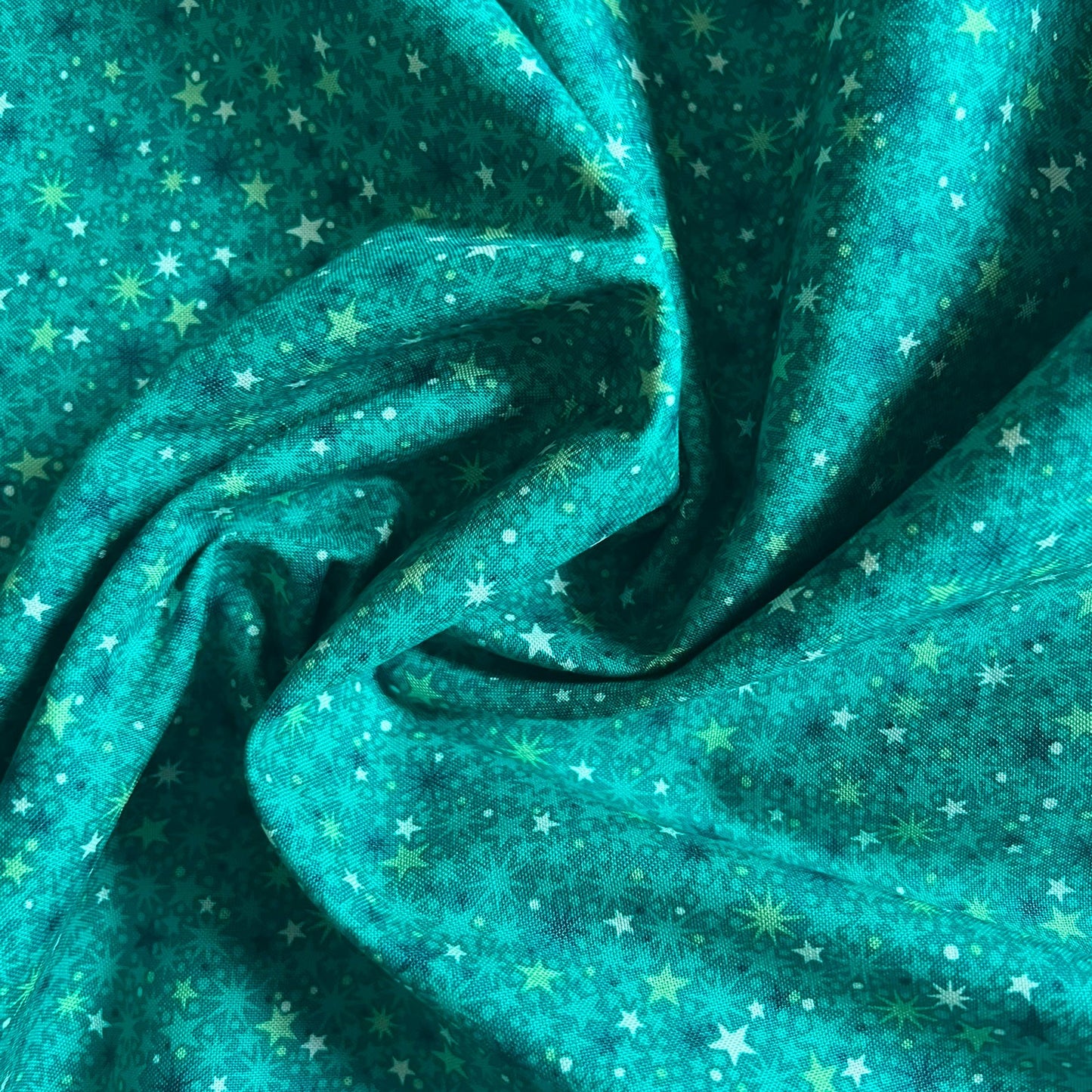 A close-up of draped teal fabric with an allover pattern of small white stars and pale yellow floral/star motifs.